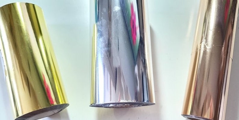 May include: Three rolls of metallic wrapping paper in gold, silver, and rose gold.