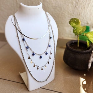 May include: A silver layered necklace with a delicate chain and a thicker chain with small silver charms and blue evil eye pendants.