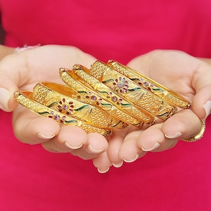 Pode incluir: Uma pilha de pulseiras de ouro com intrincados desenhos florais e detalhes em esmalte rosa e verde.
