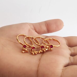 May include: Set of five gold toe rings with dangling charms and a single red gemstone on each ring.