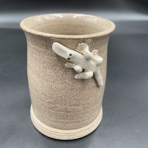May include: A beige ceramic mug with a white ceramic platypus design on the side.