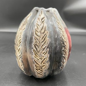May include: A black ceramic vase with a textured, leaf-like design. The vase has a rounded shape and a red accent on the side.