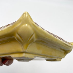 May include: A yellow ceramic planter with brown stripes. The planter has a square shape with a rounded bottom and a raised lip around the top.