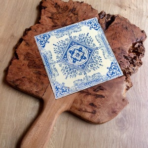 May include: A wooden serving board with a blue and white tile design. The board has a handle and is made of natural wood with a unique grain pattern.