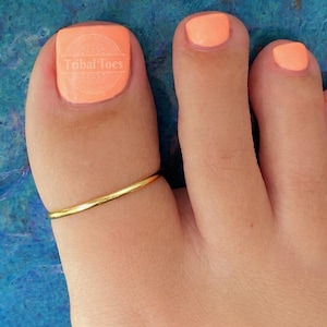 May include: Close-up of a foot with orange nail polish and a gold toe ring. The big toe has a nail sticker with the text "Tribal Toes". The other toes also have orange nail polish.