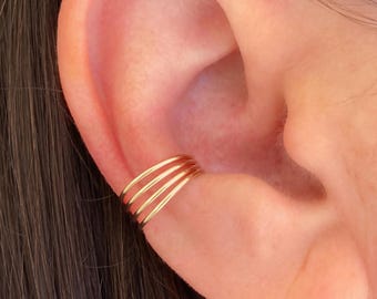May include: Gold ear cuff with four thin bands wrapped around the ear. The ear cuff is made of metal and is a simple, minimalist design.