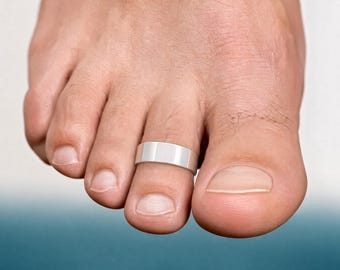 May include: A polished silver-toned toe ring featuring a smooth, flat, and wide band design. The ring is worn on the second toe, showcasing a clean, reflective metallic surface that wraps around the digit with a simple, uniform, and unadorned appearance.