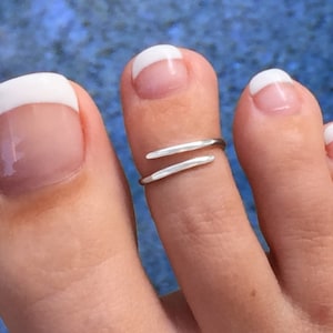 May include: A silver toe ring with a simple, double-bar design. The ring is worn on the big toe of a foot with white French manicured toenails.