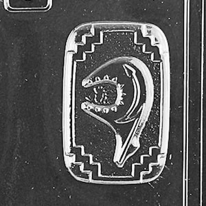 May include: A silver-toned pendant with a detailed design of a fish head with an open mouth and a row of teeth. The pendant is surrounded by a decorative border.