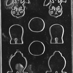 Puede incluir: Molde de plástico transparente con caras de conejito, círculos, mitones y diseños en forma de campana. El molde es para hacer chocolates o caramelos. El texto "LIFE OF THE PARTY 08886" y "FDA APPL 429" está impreso en la parte inferior.