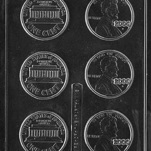 May include: A clear plastic mold for making coin-shaped chocolates. The mold features impressions of US pennies, including the Lincoln Memorial and the year 2000. The text "ONE CENT" and "UNITED STATES OF AMERICA" are visible.