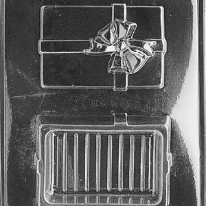 Puede incluir: Molde de plástico transparente para hacer chocolates. El molde presenta dos diseños distintos: una caja de regalo con un lazo y una forma rectangular con líneas verticales. El texto "LIFE OF THE PARTY" es visible en la parte inferior.