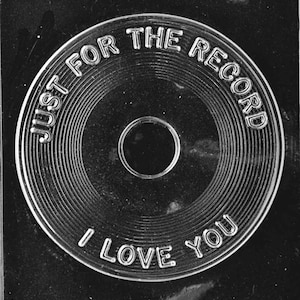 May include: A black and white plastic mold for making chocolate shaped like a record. The record has the words "Just for the record I love you" around the edge.