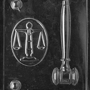 Könnte beinhalten: Eine schwarze Plastikform zum Herstellen von Schokoladennachbildungen eines Hammers und einer Justizwage. Die Form hat zwei Vertiefungen, eine für den Hammer und eine für die Waage. Die Form ist mit "Little of the Party J. 98" beschriftet.