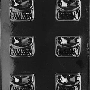 May include: A black plastic candy mold with six rectangular cavities. Each cavity has a detailed design, including a flap and textured surface, likely for chocolates or candies. The mold is designed for easy release of the treats.