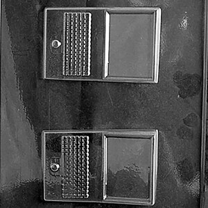 May include: A black plastic mould featuring two rectangular cavities. Each cavity has a textured section and a smooth, framed section. The mould is designed for creating shaped items, possibly for crafts or food.