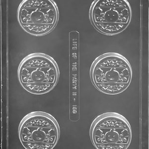May include: A clear plastic mold with six round cavities, each featuring a raised design of a pumpkin with a smiling face and wings. The mold is labeled "Life of the Party is - Lego."