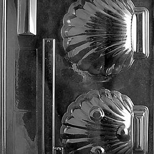 Puede incluir: Un molde de plástico transparente con diseño de concha. El molde tiene dos cavidades de concha, una cavidad rectangular y una cavidad rectangular larga y delgada. Las cavidades de concha tienen crestas detalladas y una forma de asa en el lateral.