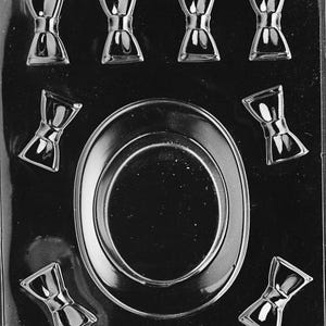 Puede incluir: Un molde de plástico transparente para hacer bombones o caramelos. El molde presenta varias formas de lazo y una forma ovalada grande. El texto "LIFE OF THE PARTY" es visible en la parte inferior del molde.