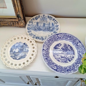 May include: Three decorative ceramic plates featuring blue and white designs. One plate commemorates the 1867-1967 Canada Centennial with a historical scene. Another has a lattice-style rim and a landscape, while the third features a floral border.