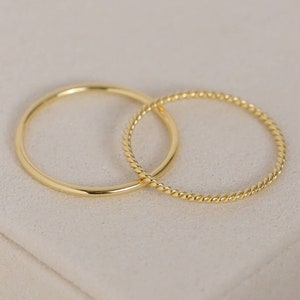May include: Two gold rings, one plain and one twisted, on a white surface.