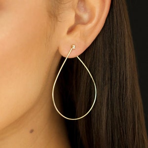 May include: A pair of gold teardrop earrings. The earrings are a simple, elegant design, with a slender, curved shape. A small, sparkling accent is at the top of the earring, near the earlobe.