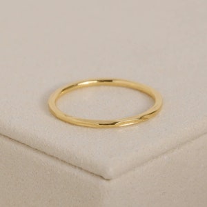 May include: A simple gold band ring with a hammered texture.