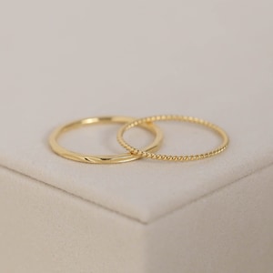 May include: Two gold rings, one with a twisted design and the other with a smooth, slightly textured surface.
