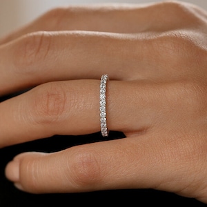 May include: A thin, silver band with a row of small, clear diamonds set in a pave setting.