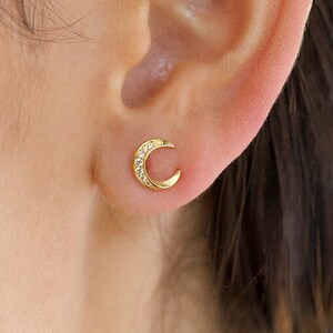 May include: A pair of gold crescent moon earrings with small clear stones set along the edge of the crescent.