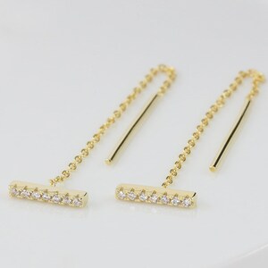 May include: A pair of gold earrings with a thin bar set with small clear stones and a dangling chain.