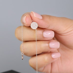 May include: A delicate silver chain bracelet with a small, round pendant encrusted with tiny white stones. The bracelet is displayed on a black box with the text "IRONY." printed on the top.