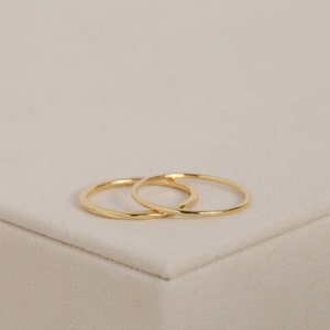 May include: Two thin gold rings, one slightly larger than the other, are stacked on top of each other. The rings are smooth and have a slightly rounded shape.