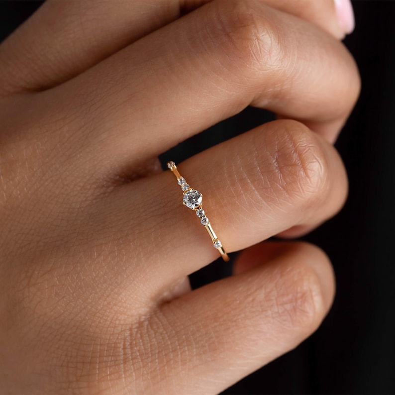 May include: A delicate gold ring with a single, round diamond in the center and smaller diamonds set along the band.