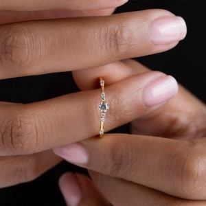 May include: A delicate gold ring with a single round diamond and smaller diamonds set along the band.