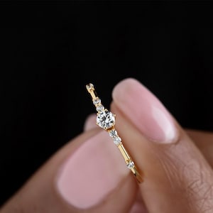 May include: A delicate gold band ring with a single round diamond and smaller diamonds set along the band.
