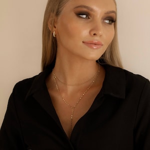K&ouml;nnte beinhalten: Eine Frau tr&auml;gt ein schwarzes Hemd mit einer goldenen mehrlagigen Halskette. Die Halskette hat eine Halskette im Choker-Stil und eine l&auml;ngere Kette mit einem Anh&auml;nger.
