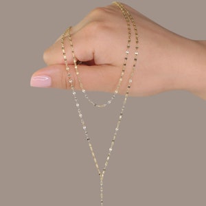 K&ouml;nnte beinhalten: Eine goldene Kettenkette mit einem zarten, gedrehten Design. Die Kette ist mit zwei Kettenstr&auml;ngen geschichtet, was einen stilvollen und eleganten Look erzeugt.
