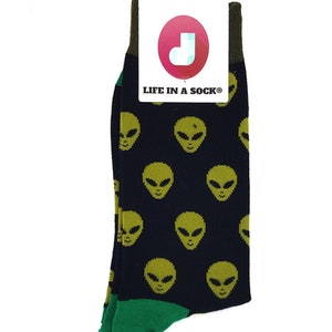 Puede incluir: Un par de calcetines negros con ribete verde y un patrón de caras de extraterrestres verdes. Los calcetines tienen una etiqueta que dice "Life in a Sock".