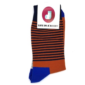 以下が含まれることがあります： オレンジとネイビーのストライプ柄の靴下で、かかととつま先がブルーです。靴下には「LIFE IN A SOCK®」という文字が書かれた白いタグと、白い「J」の文字が書かれた赤い円が付いています。