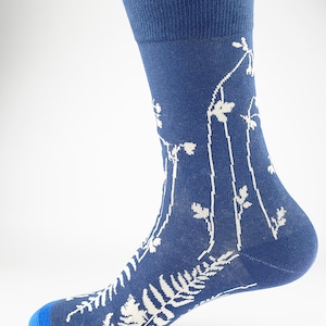 Può includere: Calzini blu con un motivo floreale bianco. I calzini hanno un polsino blu e un motivo a felce bianco sul piede.
