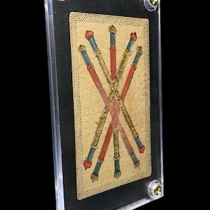Op de afbeelding: Een tarotkaart met een ontwerp van gekruiste staven in rood, goud en blauw op een beige achtergrond. De kaart wordt getoond in een transparante acrylhouder, vastgezet met goudkleurige schroeven, tegen een zwarte achtergrond.