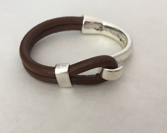 May include: A brown leather bracelet with a silver clasp. The bracelet is double-layered and has a simple design.