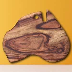 May include: A wooden cutting board shaped like the continent of Australia. The board is made of dark brown wood with a natural grain pattern. It has a hole in the top for hanging.