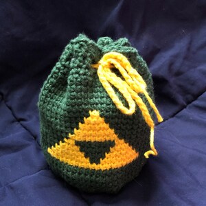 Puede incluir: Una bolsa de cordón verde hecha a crochet con un diseño de triángulo amarillo. La bolsa tiene un cordón amarillo.