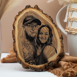 Könnte beinhalten: Eine Holzplakette mit natürlichem Rand zeigt ein lasergraviertes Porträt eines Paares. Das Bild ist detailliert und zeigt die Personen mit Brille und Hut. Das Holz hat einen warmen, natürlichen Farbton, und die Plakette wird mit dekorativen Elementen präsentiert.