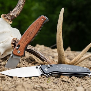 May include: Two pocket knives with personalized engravings. One knife has a wooden handle with the text "Happy Father's Day" engraved on it. The other knife has a black handle with the text "I love you - Zach" engraved on it.