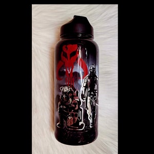 Peut inclure: Gourde noire avec un bouchon noir. Elle pr&eacute;sente un graphisme rouge et blanc d'un cr&acirc;ne Mandalorien et de deux personnages. La gourde a un fond sombre et enfum&eacute; et un dessus noir.