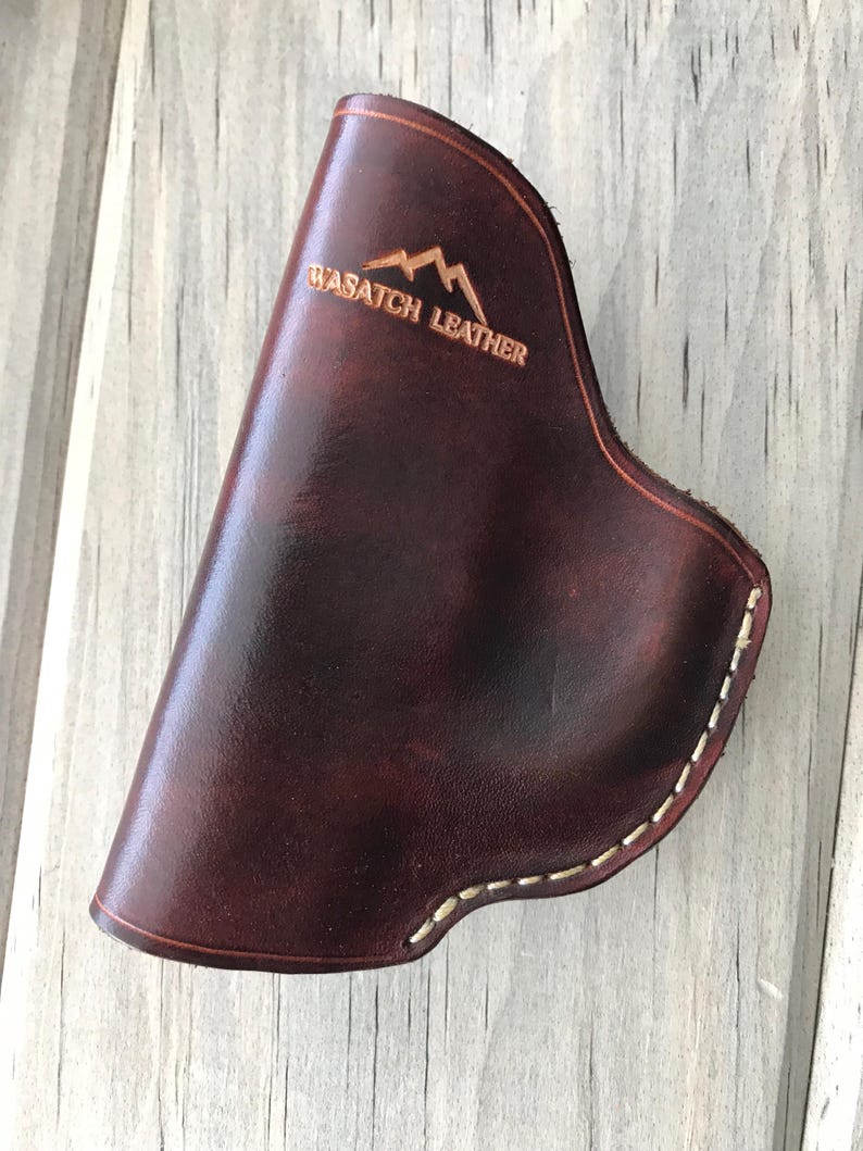 Peut inclure: Un &eacute;tui en cuir marron avec des coutures blanches et le texte "Wasatch Leather" en relief sur le devant.