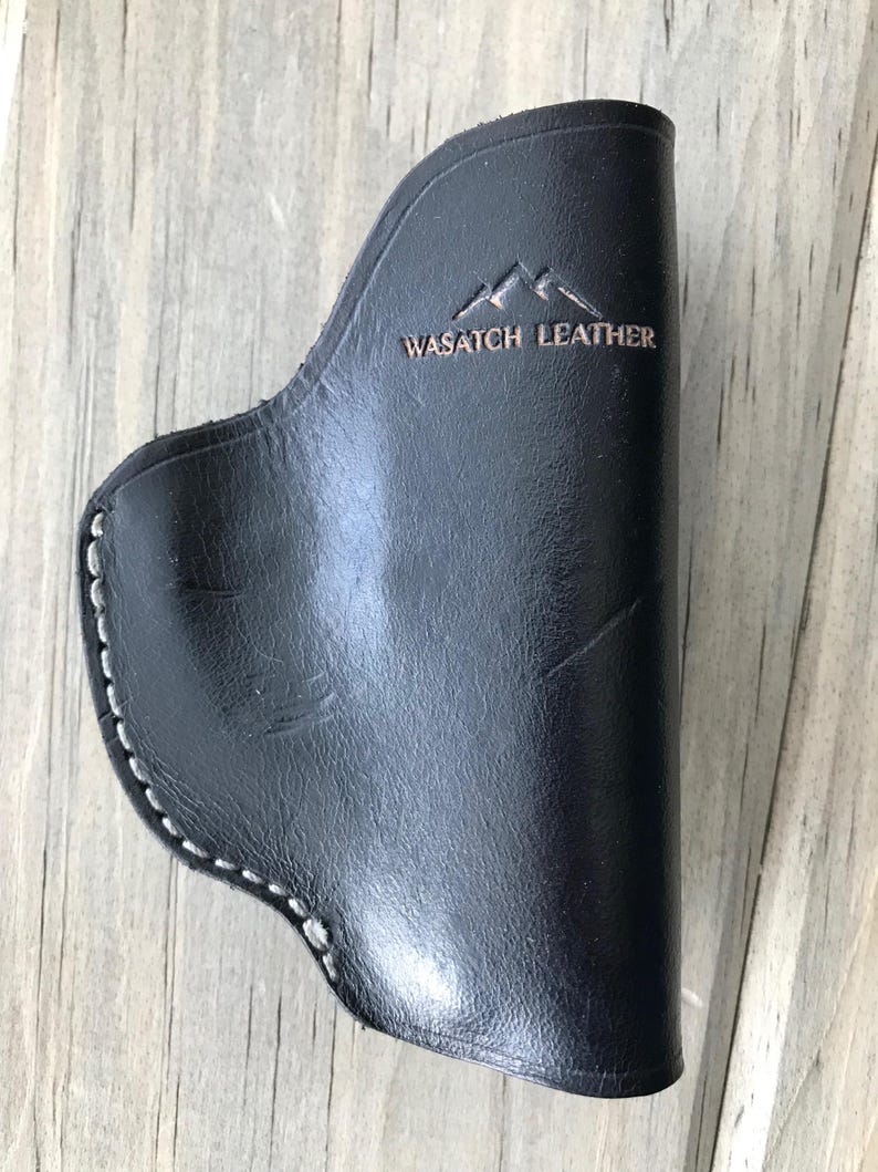 Peut inclure: Un &eacute;tui en cuir noir avec des coutures blanches et le texte "WASATCH LEATHER" en relief sur le devant.